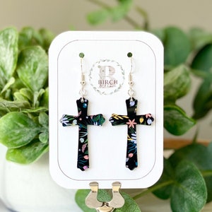 May include: A pair of black cross earrings with a floral print. The earrings are on a white display card with the text "Birch" in a circle.