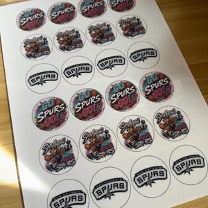 May include: A sheet of circular stickers featuring San Antonio Spurs basketball designs. The stickers include text such as Go Spurs Go, San Antonio Spurs, and Puro Pinche Spurs, alongside illustrations of a basketball-playing coyote mascot.