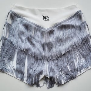 Può includere: Shorts sportivi bianchi con bordino a frangia argentata. I pantaloncini hanno un piccolo logo sul retro.