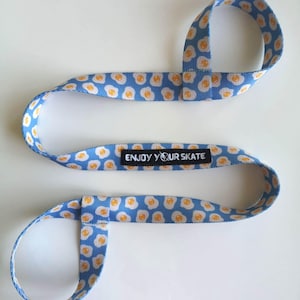 May include: Blue and yellow patterned strap with a black label that says "ENJOY YOUR SKATE".