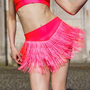 May include: A pink crop top and a pink skirt with a fringe hem. The skirt is made of a shiny fabric.