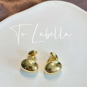 May include: A pair of gold-toned earrings with a rounded, pebble-like design. The earrings have a small, round post that attaches to the ear.