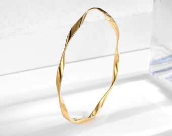 Puede incluir: Un brazalete de metal dorado retorcido. El brazalete está hecho de metal y tiene un acabado liso y pulido.
