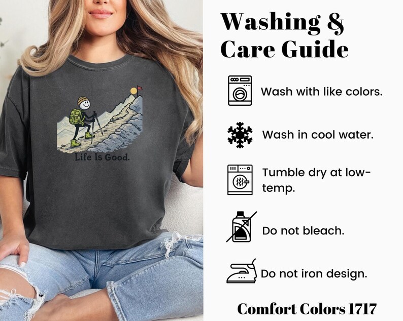 May include: Dark gray Comfort Colors t-shirt featuring a stick figure hiking up a mountain with the text "Life Is Good." The shirt also includes a washing and care guide with instructions for washing and drying. The shirt is made of Comfort Colors 1717 material.