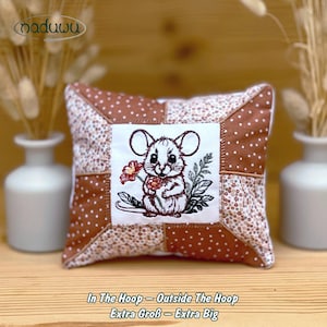 May include: A square cushion with a patchwork design in brown and white. The centre features an embroidered mouse holding flowers. The text "In The Hoop - Outside The Hoop Extra Groß - Extra Big" is at the bottom of the cushion.