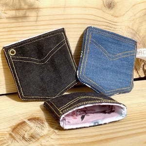 Könnte beinhalten: Drei Taschen in Form von Jeans-Taschen. Eine ist schwarz, eine blau und die dritte ist offen und zeigt ein florales Innenfutter. Alle haben gelbe Nähte und ein Taschenmuster.