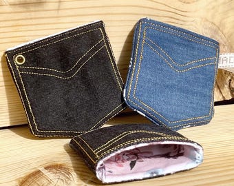 May include: Three denim-style pocket-shaped pouches. One is black, one is blue, and the third is open, revealing a floral interior. All have yellow stitching and a pocket design.