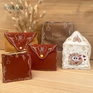Può includere: Una collezione di pochette in feltro ricamate e una busta decorativa. Le pochette sono nei toni del marrone e del rosso, con ricami a fiocco e floreali. La busta presenta un personaggio dei cartoni animati con un bastoncino di zucchero. Il testo "Frohe Weihnachten" è visibile.