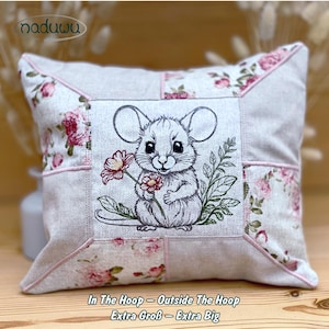 Könnte beinhalten: Quadratisches Zierkissen mit Patchwork-Design. Die Mitte zeigt eine gestickte Maus, die eine Blume hält. Florale Stoffakzente säumen die Ränder. Der Text "In The Hoop - Outside The Hoop Extra Groß - Extra Big" befindet sich unten.