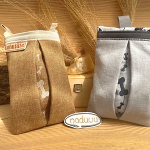 May include: Two fabric dog poop bag holders with bone designs. One is brown with white bones and the other is gray with black bones. The brown holder has the text "Lohntüte" on it.
