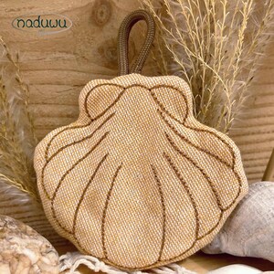 Pode incluir: Uma bolsa de tecido bege em forma de concha com uma trama texturizada e detalhes costurados em castanho ao longo das nervuras. A bolsa possui uma al&ccedil;a de cord&atilde;o castanho no topo para pendurar. A marca naduwu est&aacute; impressa no canto superior.