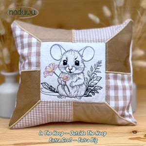 Könnte beinhalten: Quadratisches Zierkissen mit Patchwork-Design. Die Mitte zeigt eine gestickte Maus, die Blumen hält. Das Kissen hat ein beige-weißes Vichy-Muster, braunen Wildlederstoff und den Text "In The Hoop - Outside The Hoop Extra Groß - Extra Big".