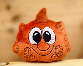 Puede incluir: Un peluche naranja con una cara sonriente, ojos blancos grandes y pupilas negras. El juguete tiene una superficie texturizada y una pequeña parte superior puntiaguda. La marca "naduuu" es visible en la esquina superior izquierda.