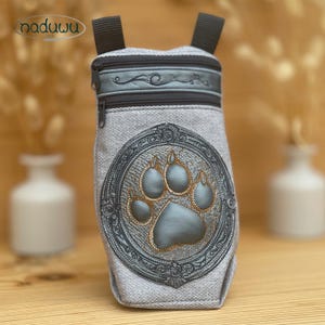 May include: A gray pet treat bag with a paw print design. The bag has a zippered top and a decorative embroidered paw print in a circular frame. The bag has two black straps and the brand name "naduuu" is visible.