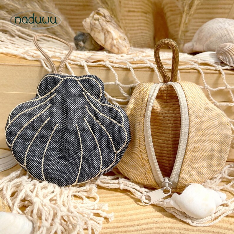 Pode incluir: Duas bolsas em forma de concha com al&ccedil;as para pendurar. Uma &eacute; de ganga azul escura com linhas costuradas a branco, e a outra &eacute; de tecido texturizado bege claro com um fecho de correr vertical central. A marca naduwu &eacute; vis&iacute;vel no canto.