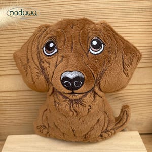 May include: A brown plush dog toy with embroidered details. The toy has large, expressive eyes, a black nose, and a slightly open mouth. The dog's fur is a soft, textured material. The toy is designed to resemble a dachshund.
