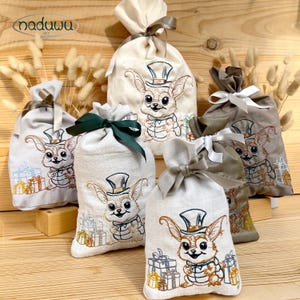 Peut inclure: Six sacs cadeaux en tissu de tons neutres, chacun orné d'un lapin de dessin animé brodé portant un chapeau haut de forme et tenant des cadeaux. Les sacs sont noués avec des rubans de couleurs assorties.