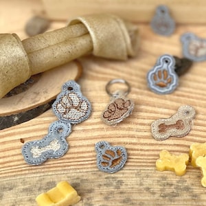 May include: Assortment of dog-themed fabric patches with paw prints and bone designs in beige and blue colors. The patches are on a wooden surface with a beige dog chew toy.