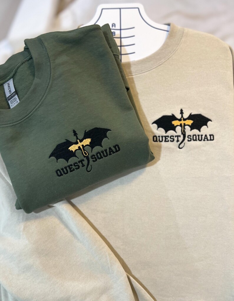 May include: Two sweatshirts, one in olive green and one in beige, both featuring an embroidered black dragon with gold accents and the text "QUEST SQUAD".