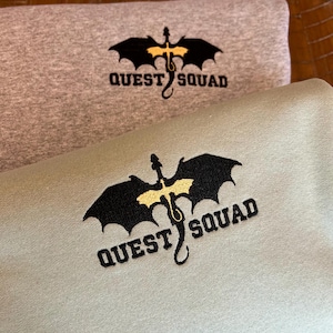 May include: Two sweatshirts with a black dragon graphic and the text "QUEST SQUAD" embroidered in yellow. The top sweatshirt is gray and the bottom sweatshirt is green.