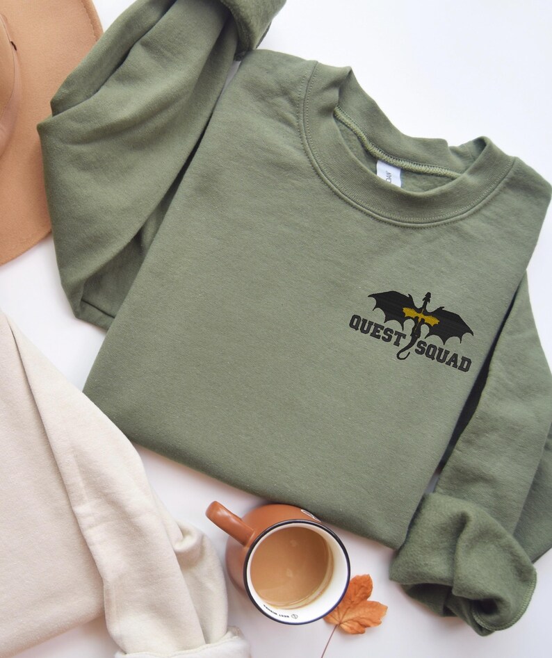 May include: A green sweatshirt with a black dragon graphic and the text "QUEST SQUAD" on the front.