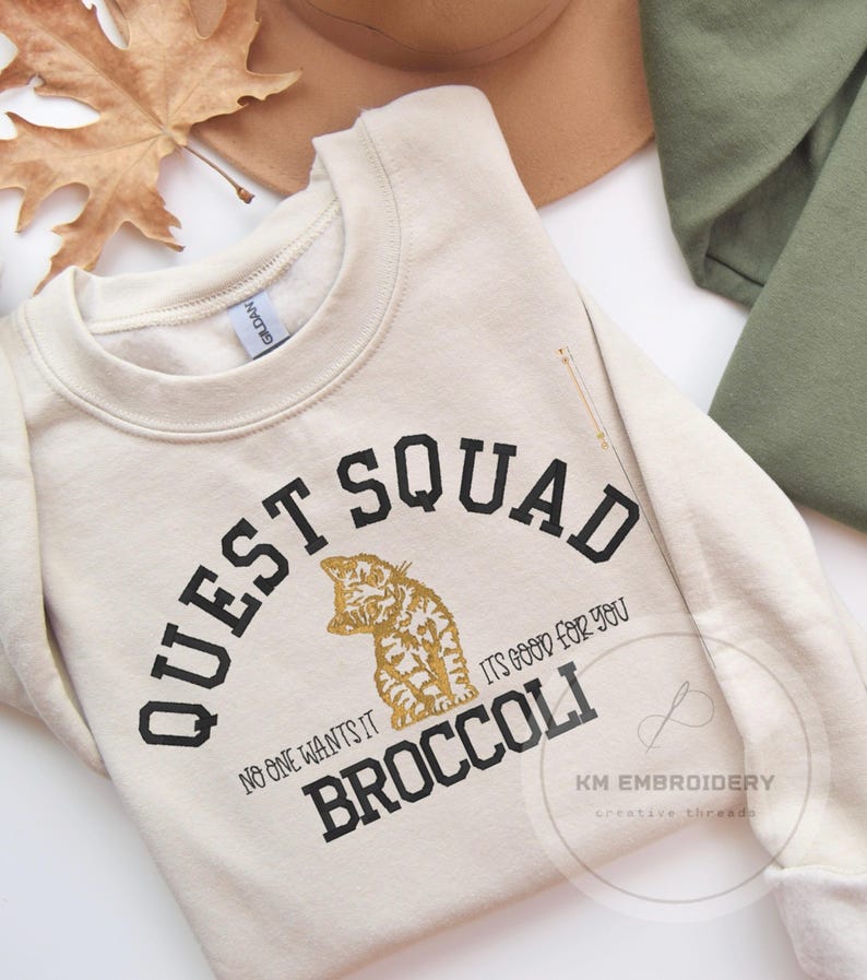 May include: A cream colored sweatshirt with black text that reads "Quest Squad" and "No one wants it, it's good for you, Broccoli". The text is surrounded by a black circle. A gold glitter cat is in the center of the circle.