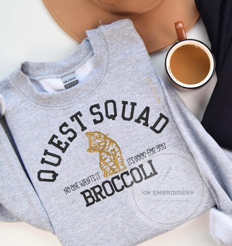 May include: Gray sweatshirt with black text that reads "Quest Squad" and "No one wants it, it's good for you Broccoli". A gold cat illustration is in the center of the text.