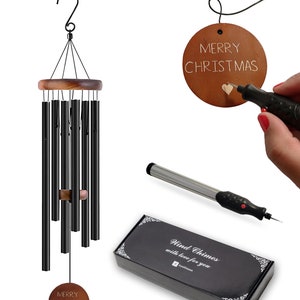 May include: A black metal wind chime with wooden accents and eight tubes. The chime is hanging from a hook. A wooden round ornament with the text "Merry Christmas" is being engraved with a small electric tool. The ornament is also included in the package. The package is black with white text that reads "Wind Chimes with love for you".