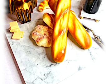 Könnte beinhalten: Ein weißes Marmor-Servierbrett mit drei goldbraunen Brötchen und einem kleinen weißen Brötchen mit Zuckerkristallen darauf. Außerdem befinden sich kleine Quadrate aus weißem Käse auf dem Brett.