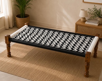 May include: A low-profile bench featuring a rectangular frame made of dark brown turned wooden legs. The seat is constructed from woven black and white cord arranged in a repeating zigzag chevron pattern, with white cord accents at both ends.