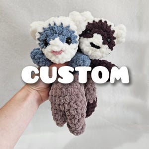 May include: Two handmade crochet animal plushies. One is blue and white, the other is dark purple and white. Both have black eyes and pink smiles. The word "CUSTOM" is overlaid on the image.