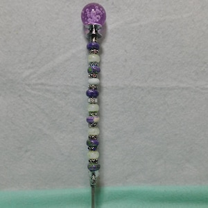 May include: A purple and white beaded wand with a clear glass orb at the top. The orb has small air bubbles inside.