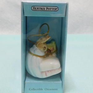 May include: A Beatrix Potter collectible ornament featuring a small rabbit figure in a white and blue outfit, housed in a light blue rectangular box with the text Beatrix Potter and Collectible Ornament printed on the front.