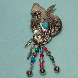 May include: A silver tone brooch with a turquoise stone and dangling beads in red, green, blue, and white. The brooch has a feather design and a bell charm.