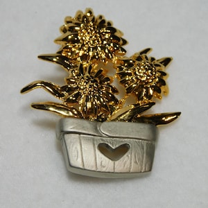 May include: Gold tone flower brooch with three flowers in a silver tone pot with a heart cut out.