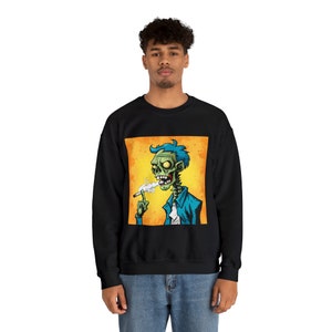 Könnte beinhalten: Schwarzes Sweatshirt mit einem Grafikdruck eines grünen Zombies mit blauen Haaren, der auf einem gelben Hintergrund eine Zigarette raucht.