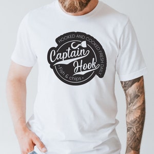 May include: White t-shirt with a black and white logo that says "Hooked and Cooked Fresh Daily Captain Hook Fish & Chips".
