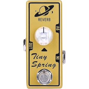 Può includere: Pedale per effetti per chitarra dorato con le scritte "REVERB" e "Tiny Spring". Il pedale ha una grande manopola trasparente, un interruttore a pedale argentato e jack di ingresso/uscita. Una grafica del pianeta è sopra la parola "REVERB".