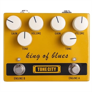 Puede incluir: Pedal de efectos de guitarra amarillo con el texto "king of blues" y "TONE CITY" en la parte delantera. El pedal tiene cuatro perillas etiquetadas como "GAIN", "VOLUME", "TONE" y "VOLUME" y dos interruptores de pedal etiquetados como "ENGINE B" y "ENGINE A".