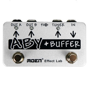 May include: A silver ABY+BUFFER guitar pedal with black lettering and two knobs. The pedal has three inputs labelled OUT A, OUT B, and TUNER, and one output labelled IN. The pedal is made by MOEN Effect Lab.