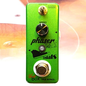 Puede incluir: Pedal de efectos de guitarra verde con una perilla negra etiquetada como "Speed" y un botón blanco etiquetado como "True Bypass". El pedal tiene el texto "phaser pedals" impreso en negro.