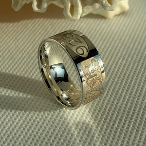 Peut inclure: Une bague en argent avec des accents rectangulaires dorés. La bague porte le numéro "925" gravé. La bague est posée sur une surface blanche.