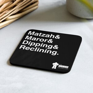 May include: Black square coaster with white text that reads "Matzah & Maror & Dipping & Reclining."  The bottom right corner has a white logo with a stick figure and the text "The Golem Museum."