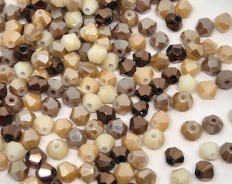 May include: A collection of faceted beads in various shades of brown, beige, and cream. The beads have a multi-faceted design, reflecting light. These beads are suitable for jewelry making and crafting projects.