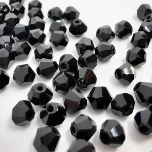 May include: A scattering of black faceted glass beads, each with a small hole for stringing. The beads are arranged in a random pattern on a white surface.