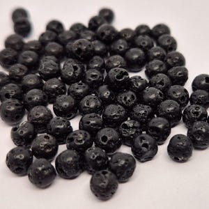May include: A close-up of a pile of black lava rock beads. The beads are round and have a rough, textured surface.