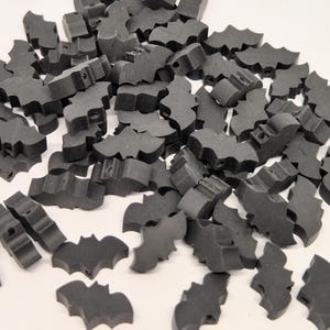 May include: A pile of small, dark gray bat-shaped wooden beads. Each bead has a hole for stringing and is designed with a bat silhouette. These beads are suitable for crafting and jewelry making.