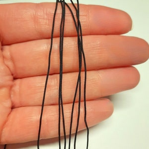 May include: A close-up of a bundle of black elastic cord, held in a hand. The cord is thin and flexible, and appears to be made of a synthetic material.