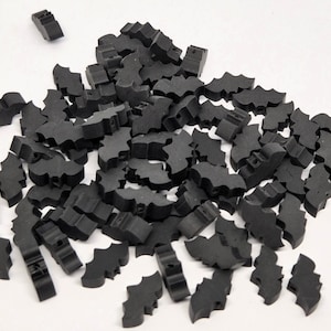 May include: A pile of small, black bat-shaped craft pieces scattered on a white surface. The bats have a simple, stylized design, with cut-out wings and a small body. These pieces are likely used for crafting or decoration.