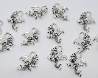 May include: Twelve silver dragon charms with intricate details. Each charm features a dragon with wings outstretched and a curled tail. The charms are perfect for adding a touch of fantasy to jewelry or crafts.